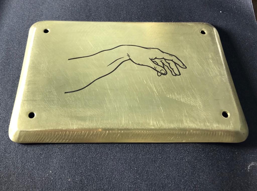 Plaque de laiton brossé portant le dessin d'une main tracé en traits fins et sombres