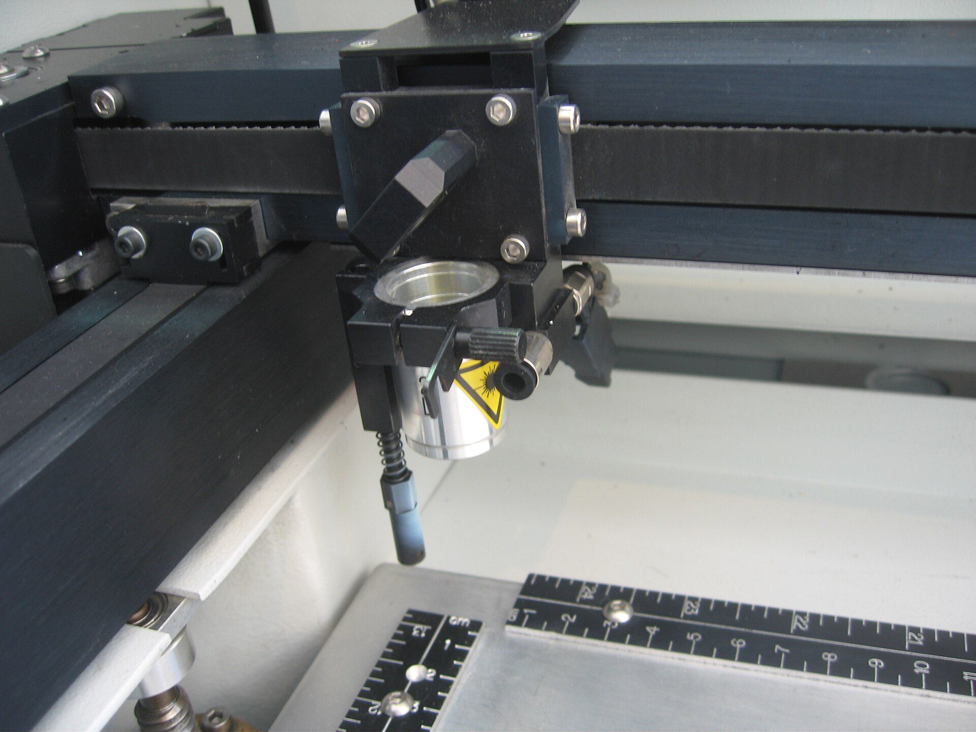 Tête de gravure d'une machine laser au-dessus d'un plateau métallique, règle graduée posée sur le plateau