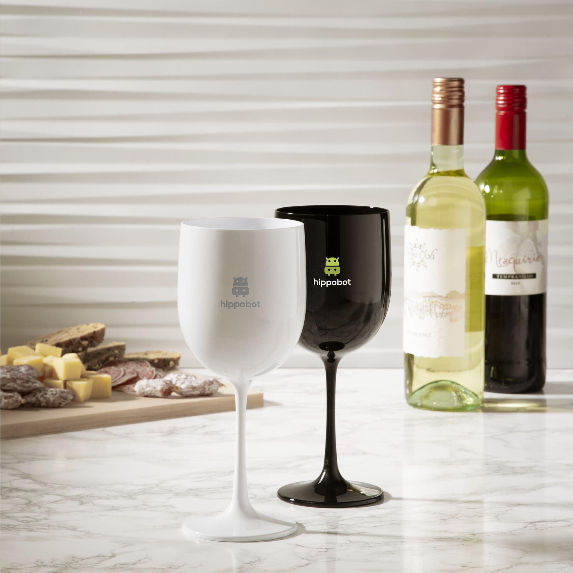 Verres à vin en plastique blanc et noir marqués d'un logo, à côté de deux bouteilles