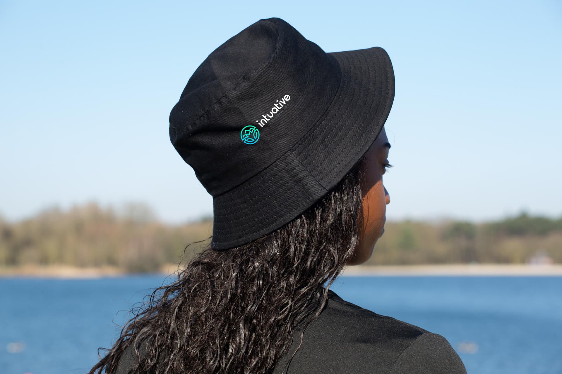 Chapeau bucket noir marqué d'un logo, porté au bord d'un lac
