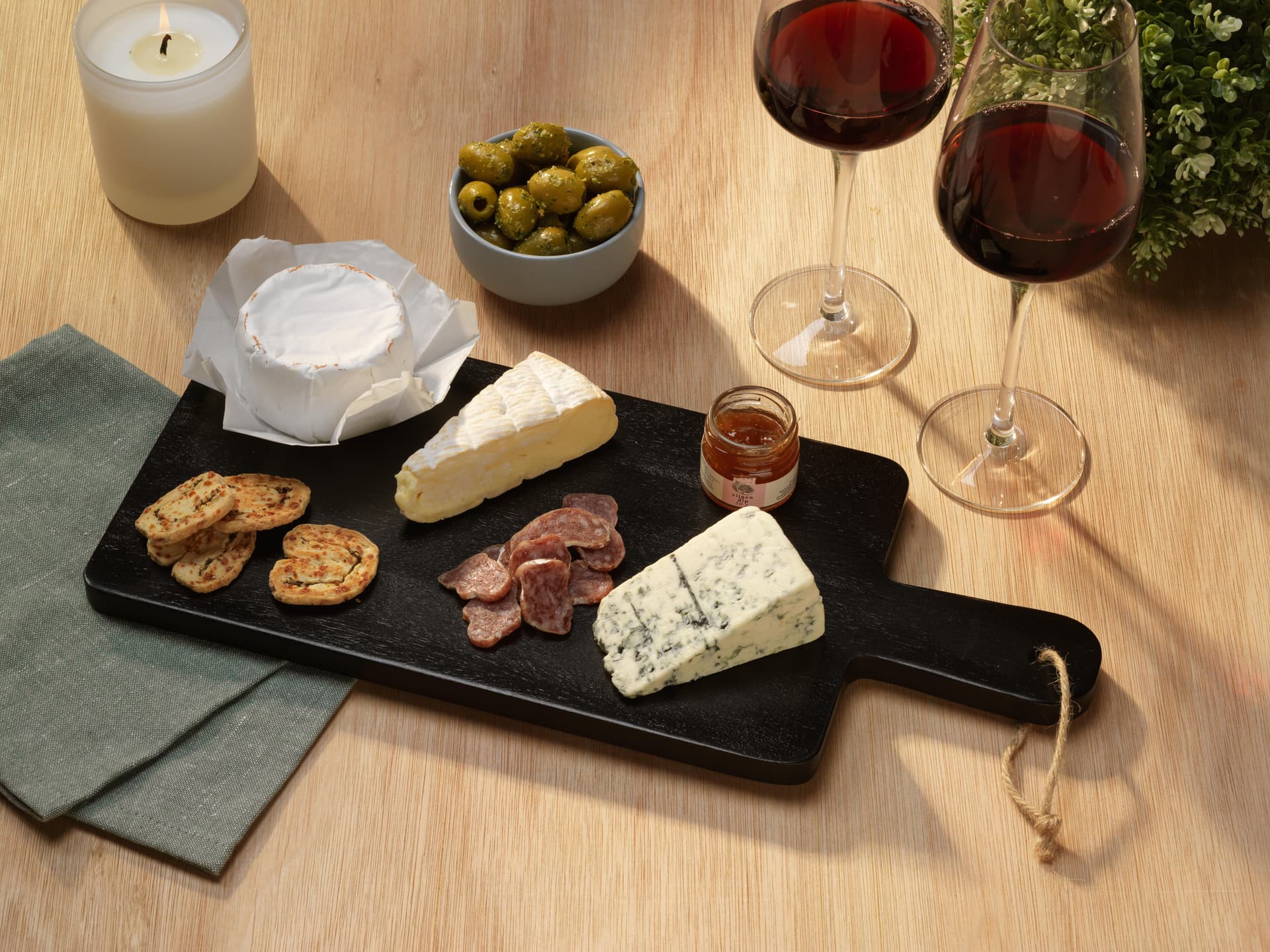 Planche de service en acacia garnie de fromages et de charcuterie, avec des verres de vin