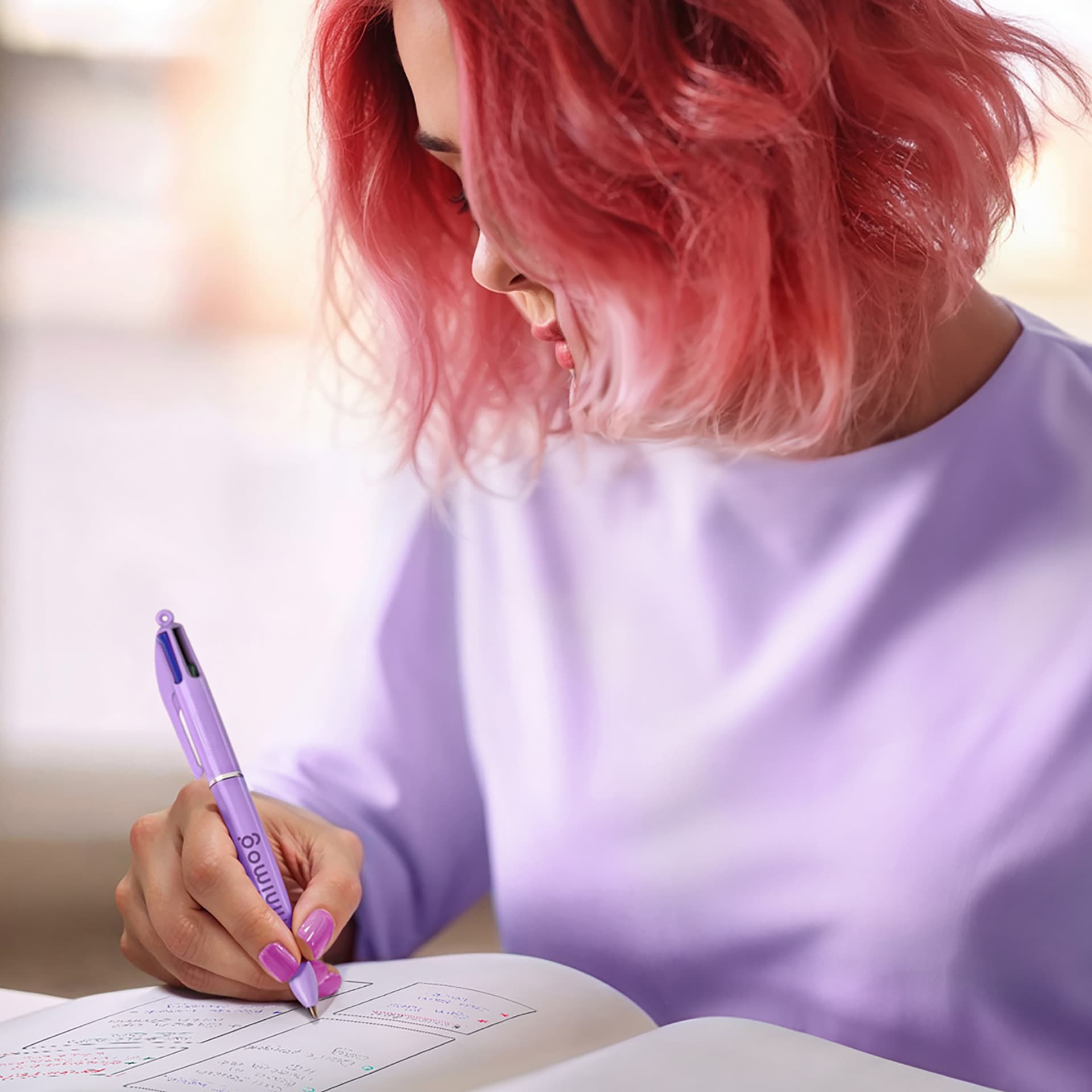 Jeune femme écrivant dans un cahier avec un stylo quatre couleurs