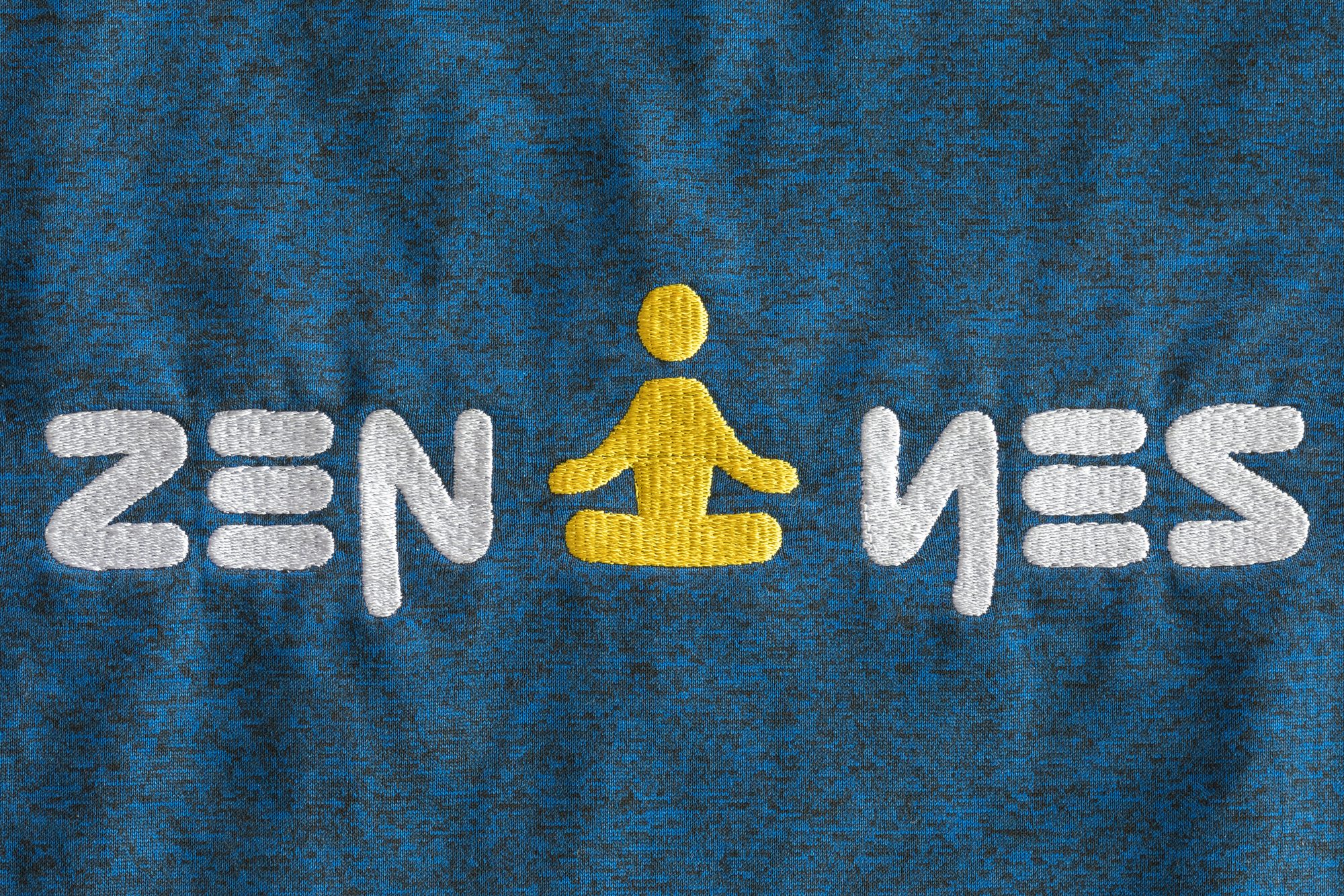 Mot ZEN YES en ambigramme brodé en fil blanc sur T-shirt bleu, avec une figure de méditation jaune au centre.