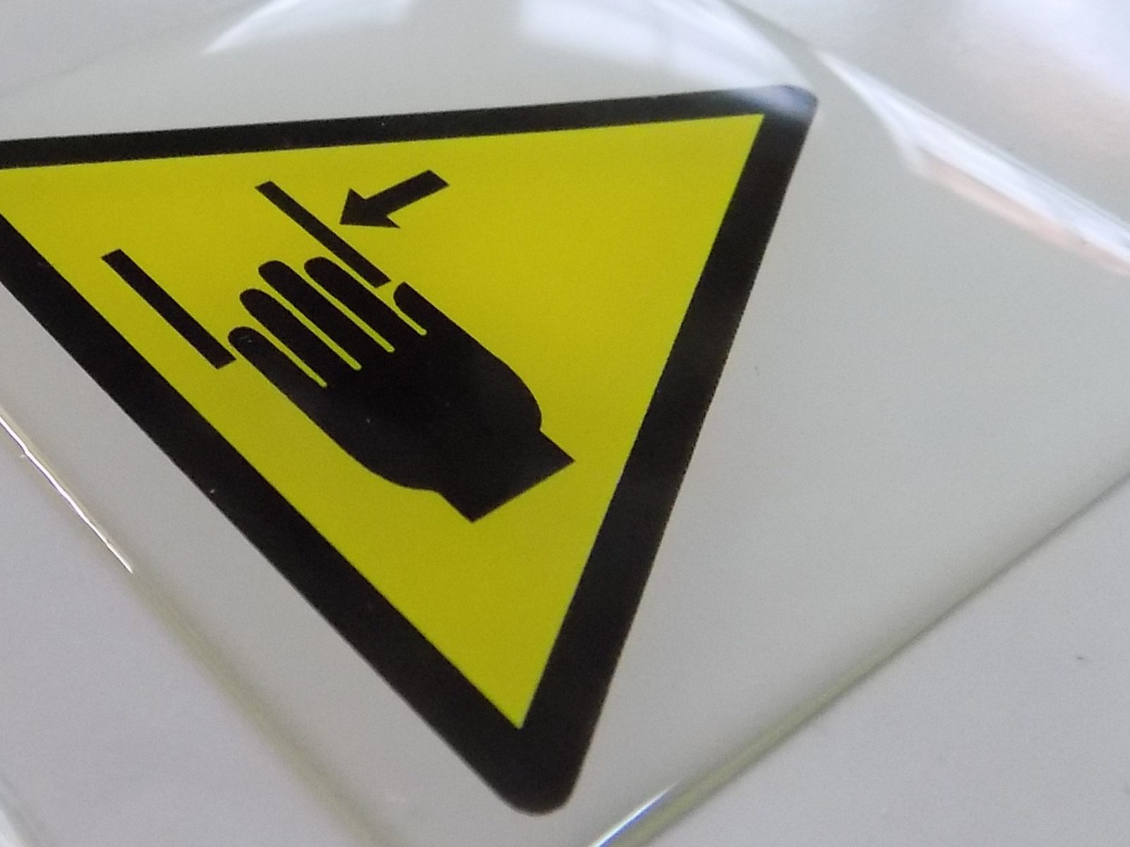 Gros plan sur un autocollant jaune à pictogramme noir, dont le dôme de résine transparente reflète la lumière.