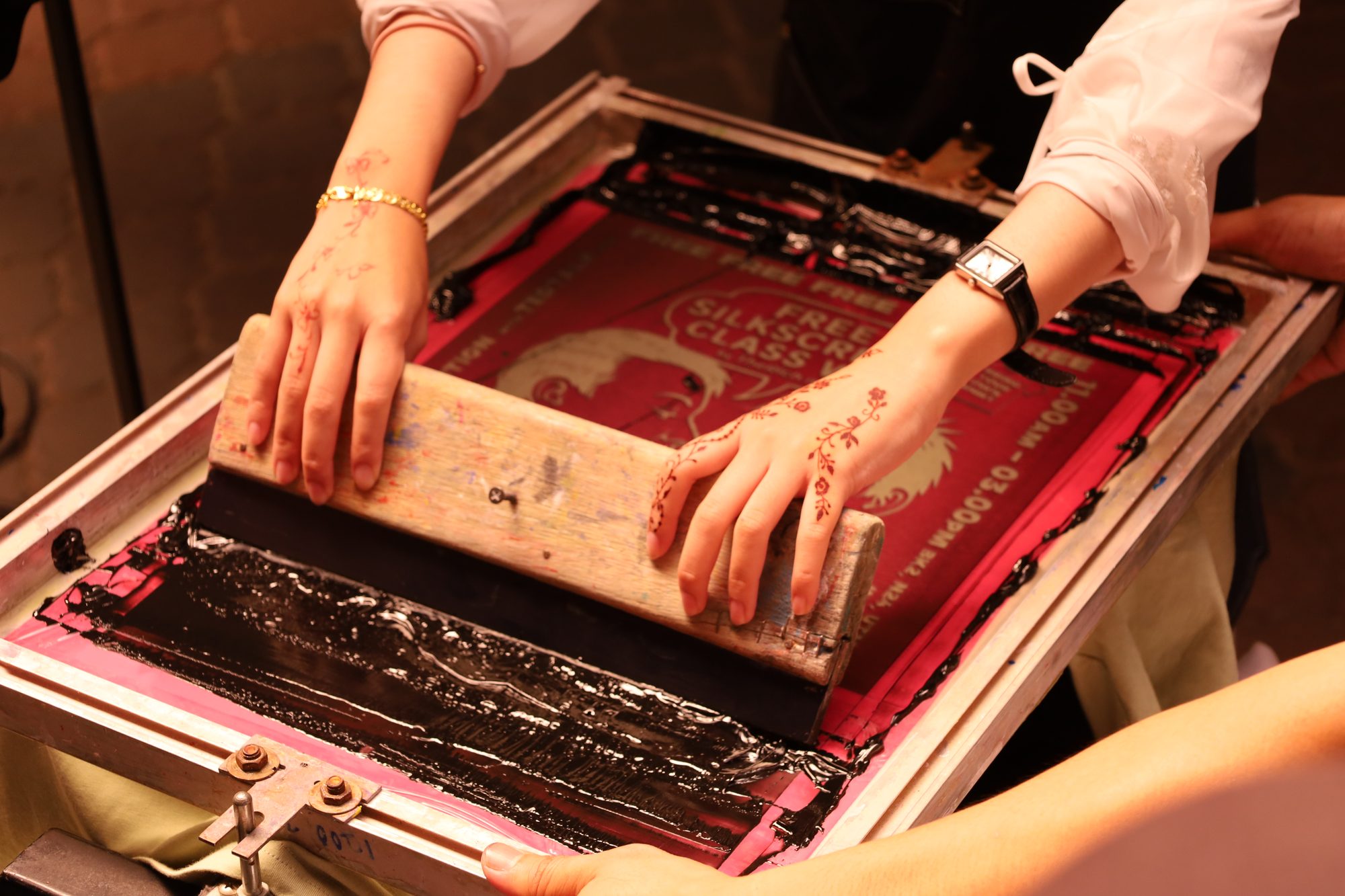 Mains tenant une raclette sur un cadre de sérigraphie, encre étalée sur l'écran.