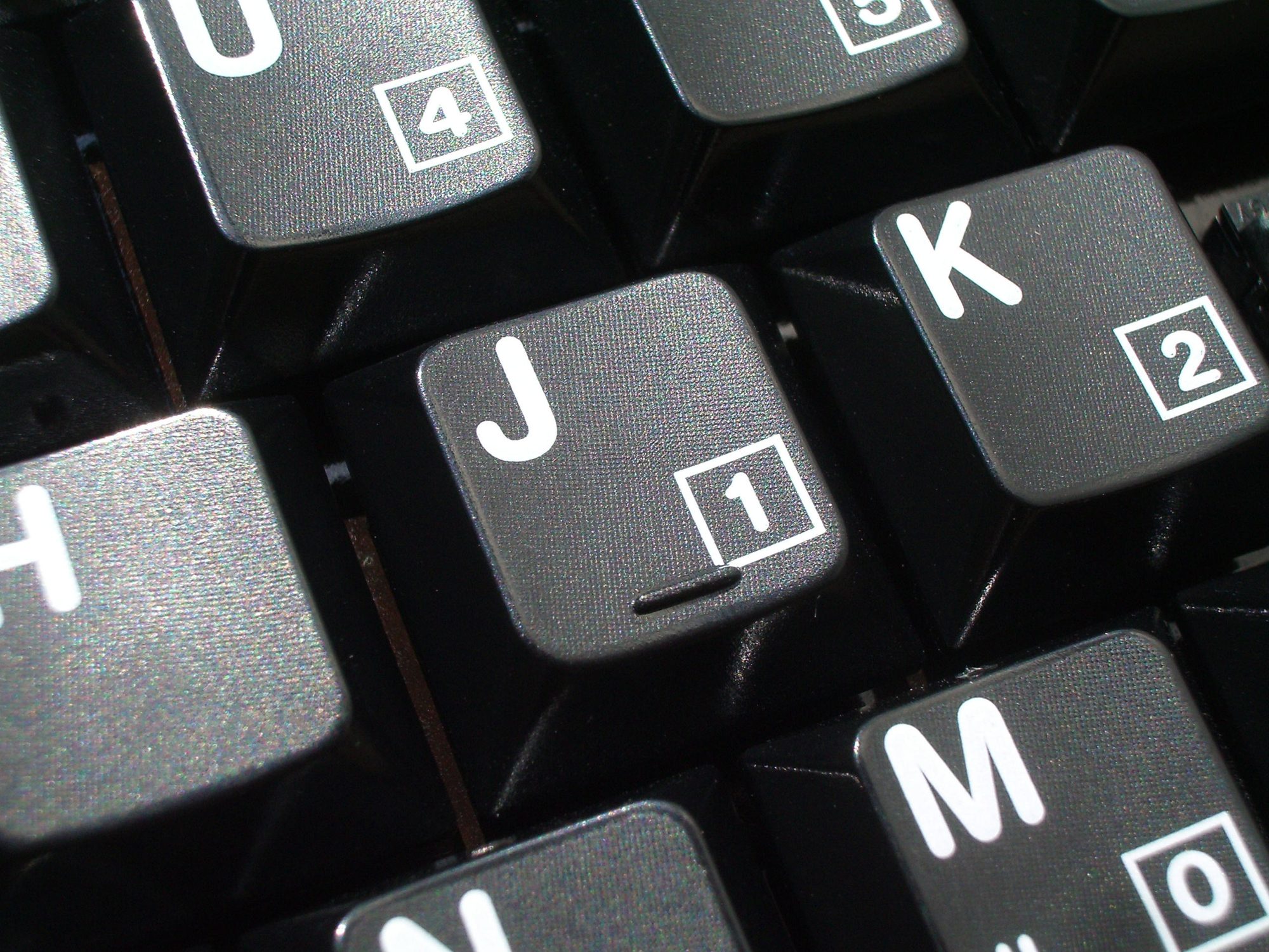 Plusieurs touches de clavier noires vues de près, lettres et chiffres imprimés en blanc (J, K, M, 1, 2).